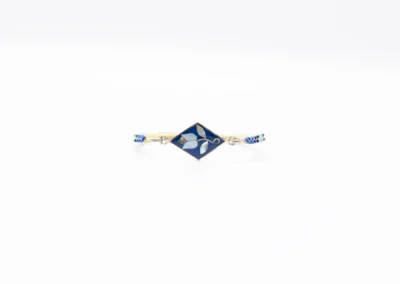 A delicate bracelet featuring a blue diamond-shaped charm with floral design, complemented by a braided blue and white band.